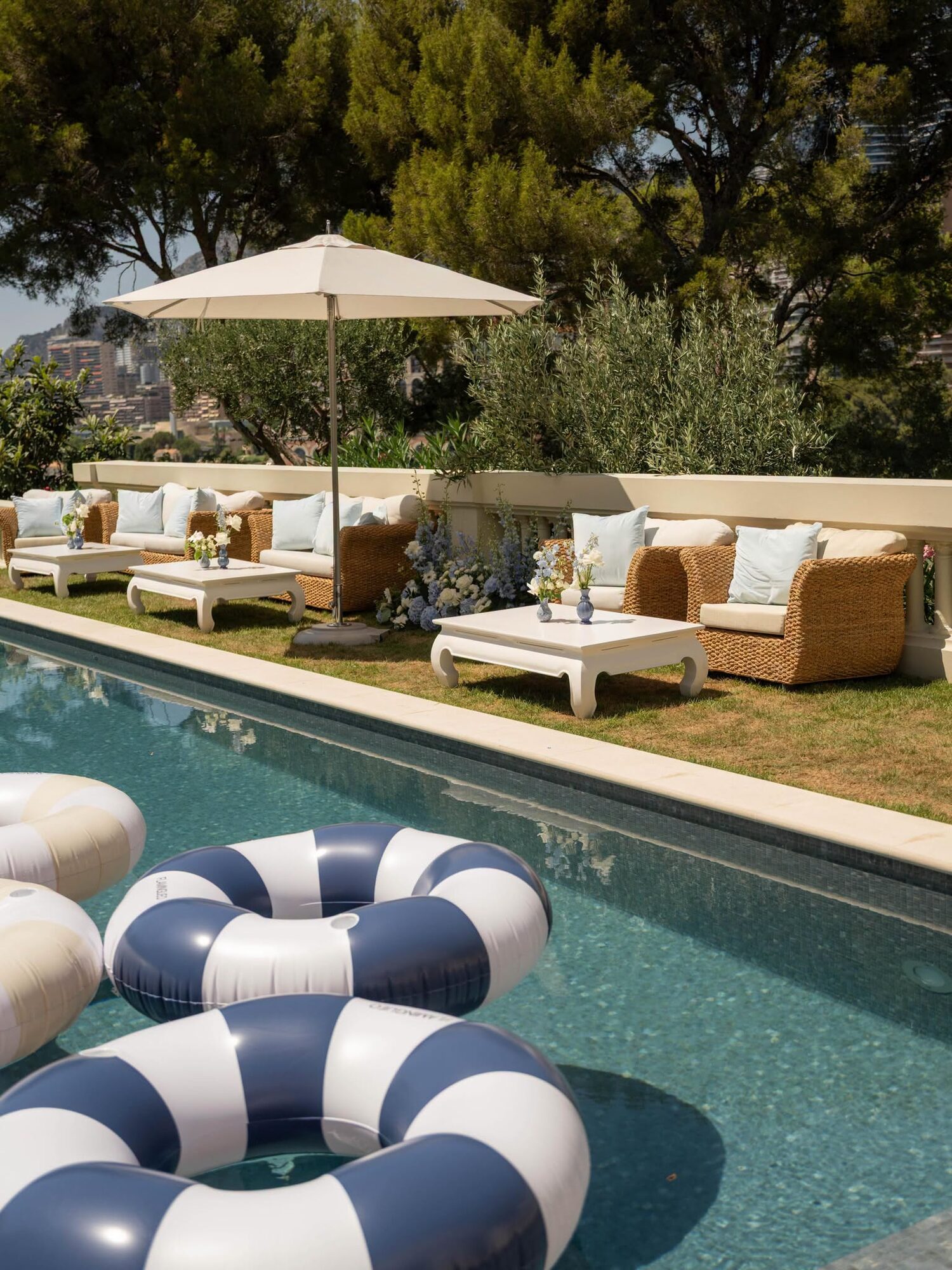 A pool in Monte-Carlo with navy and white striped floats under olive trees