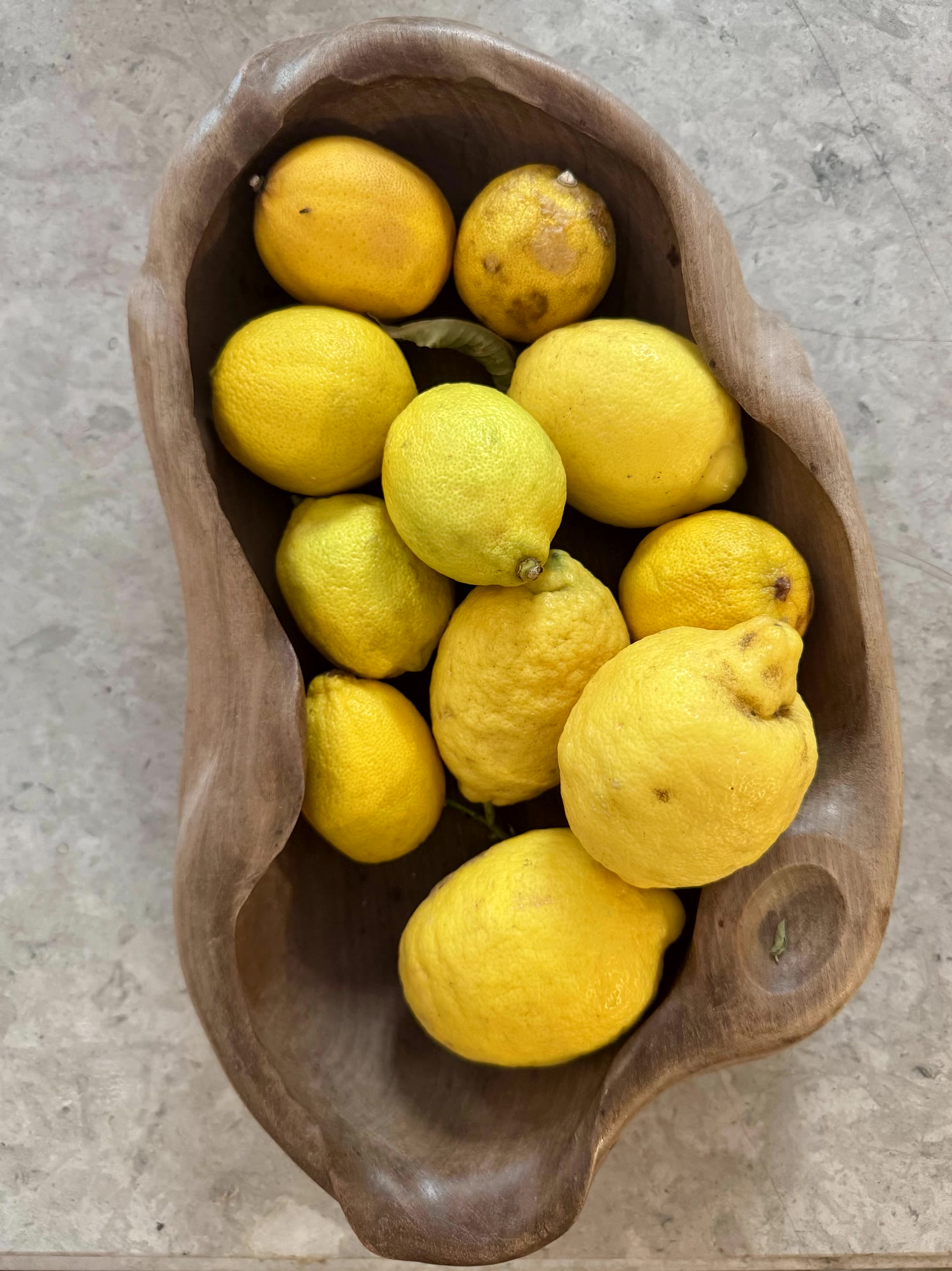 Lemons in a carved wooden bowl on stone