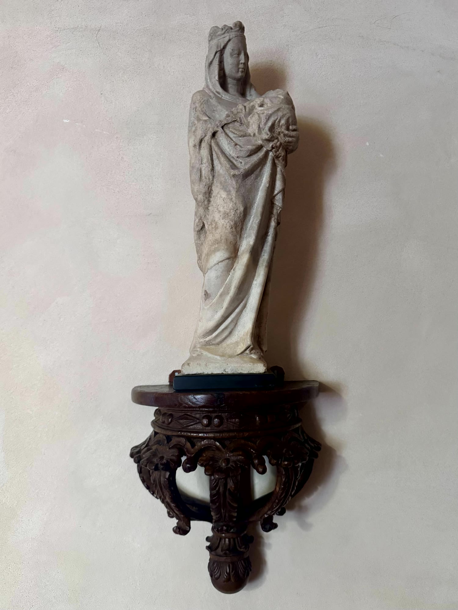 A stone Madonna on a carved wooden bracket against lime plaster