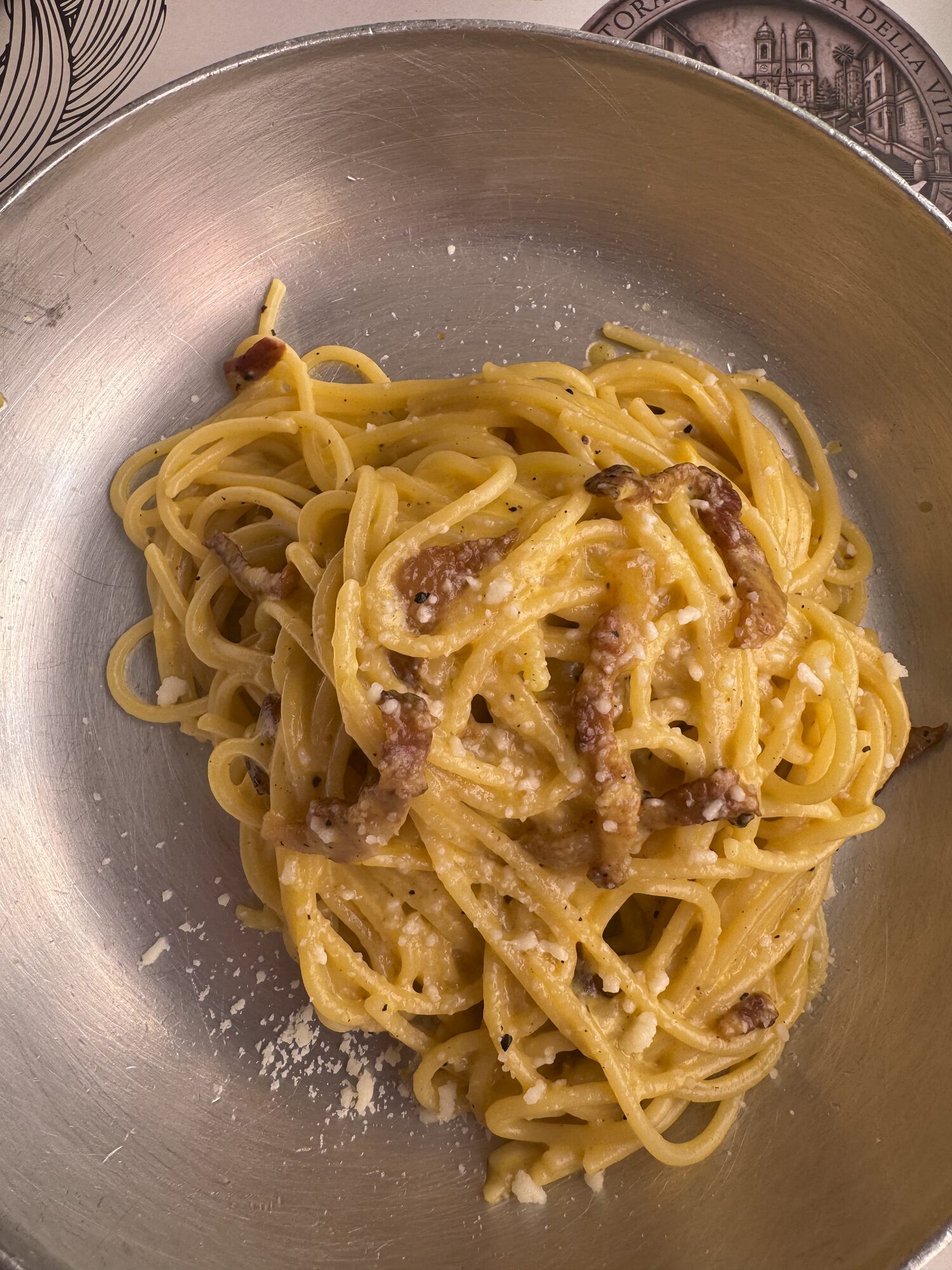 A bowl of carbonara resting on an engraved pewter plate