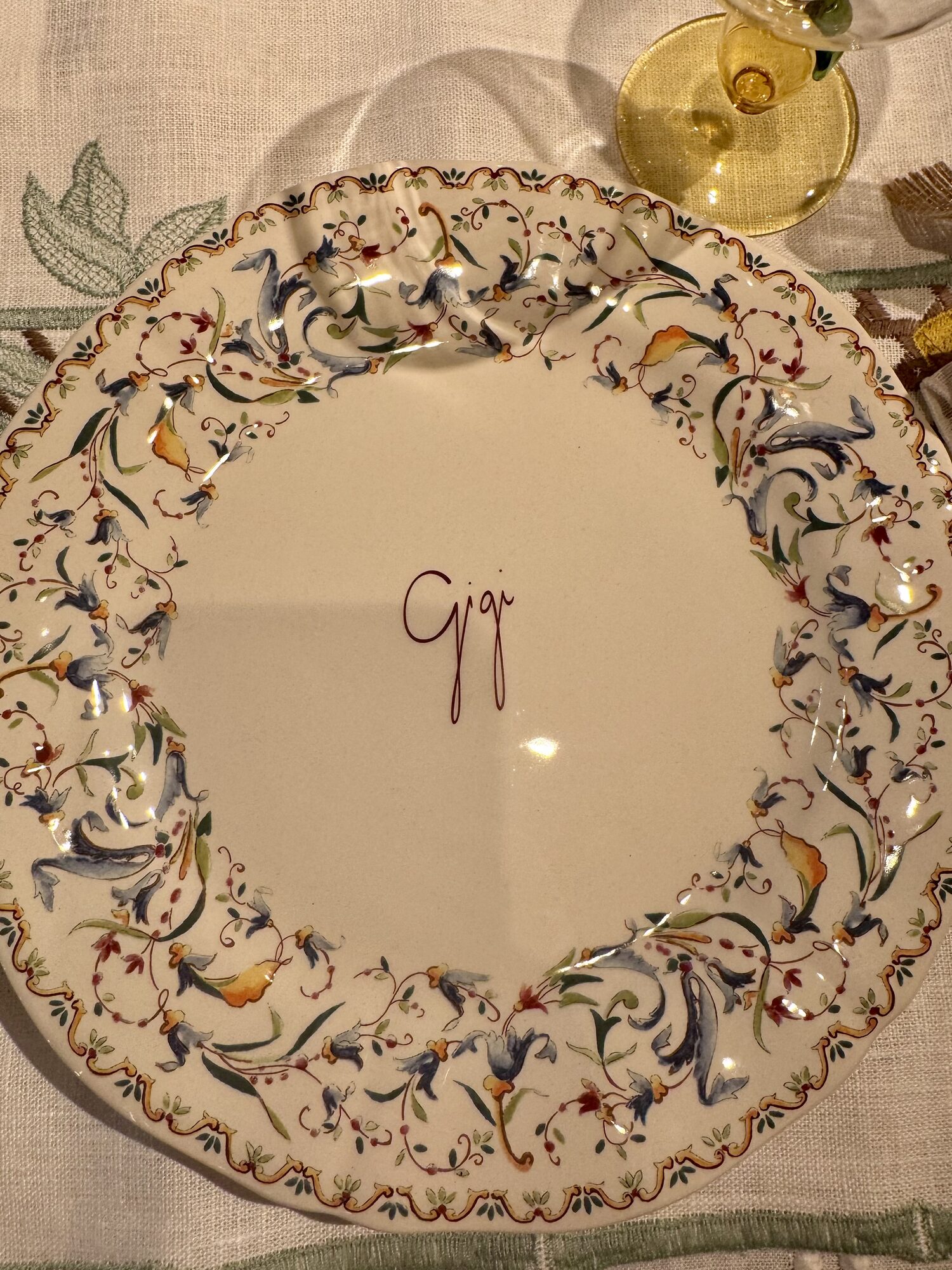 A hand-painted ceramic plate monogrammed Gigi, laid on lemon linen