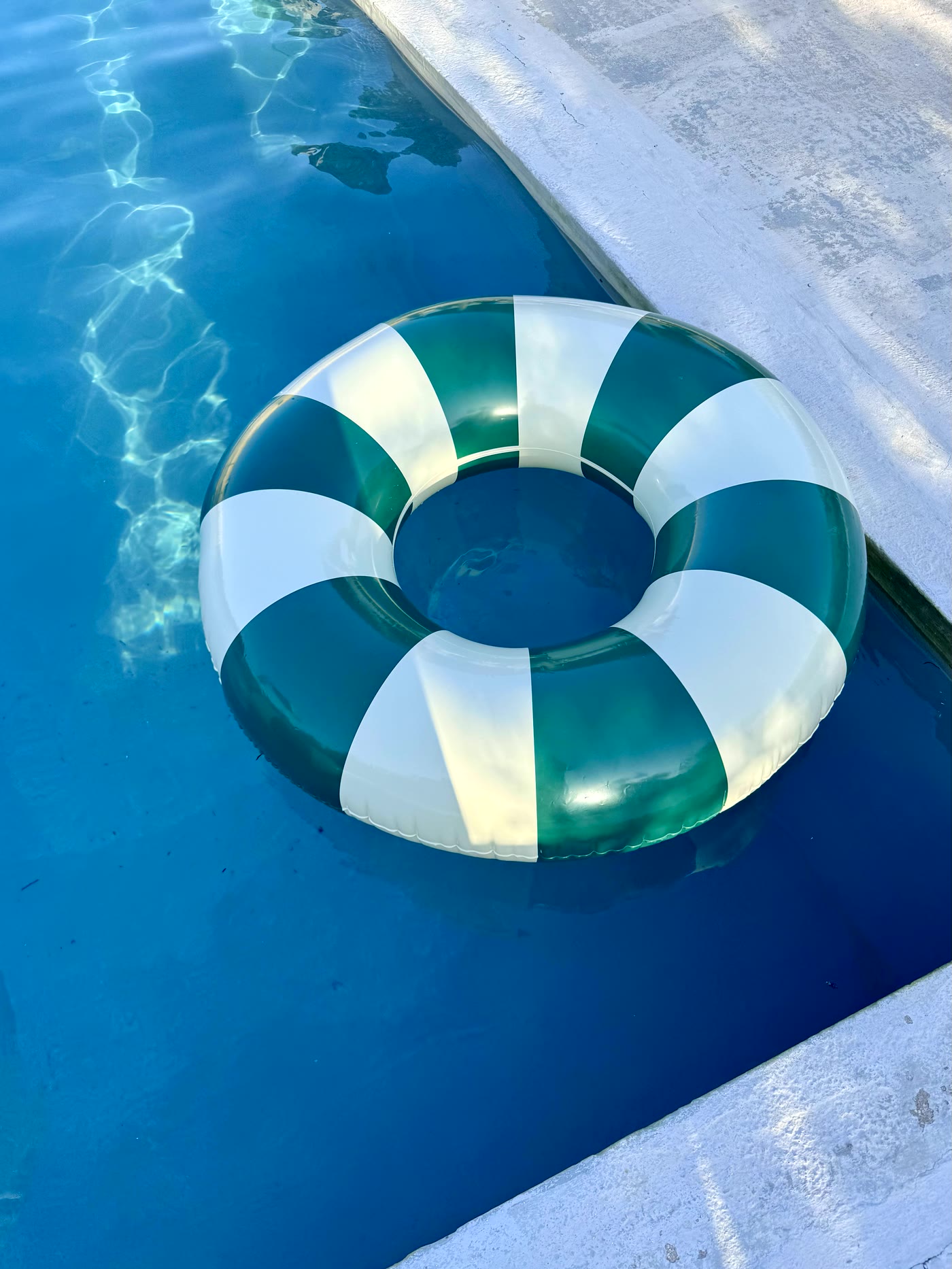 A green and white striped swim ring floating on deep blue pool water