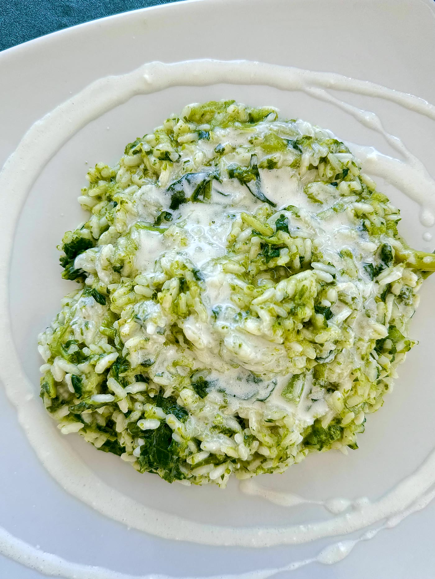 A plate of green zucchini rice under a veil of cream on white ceramic